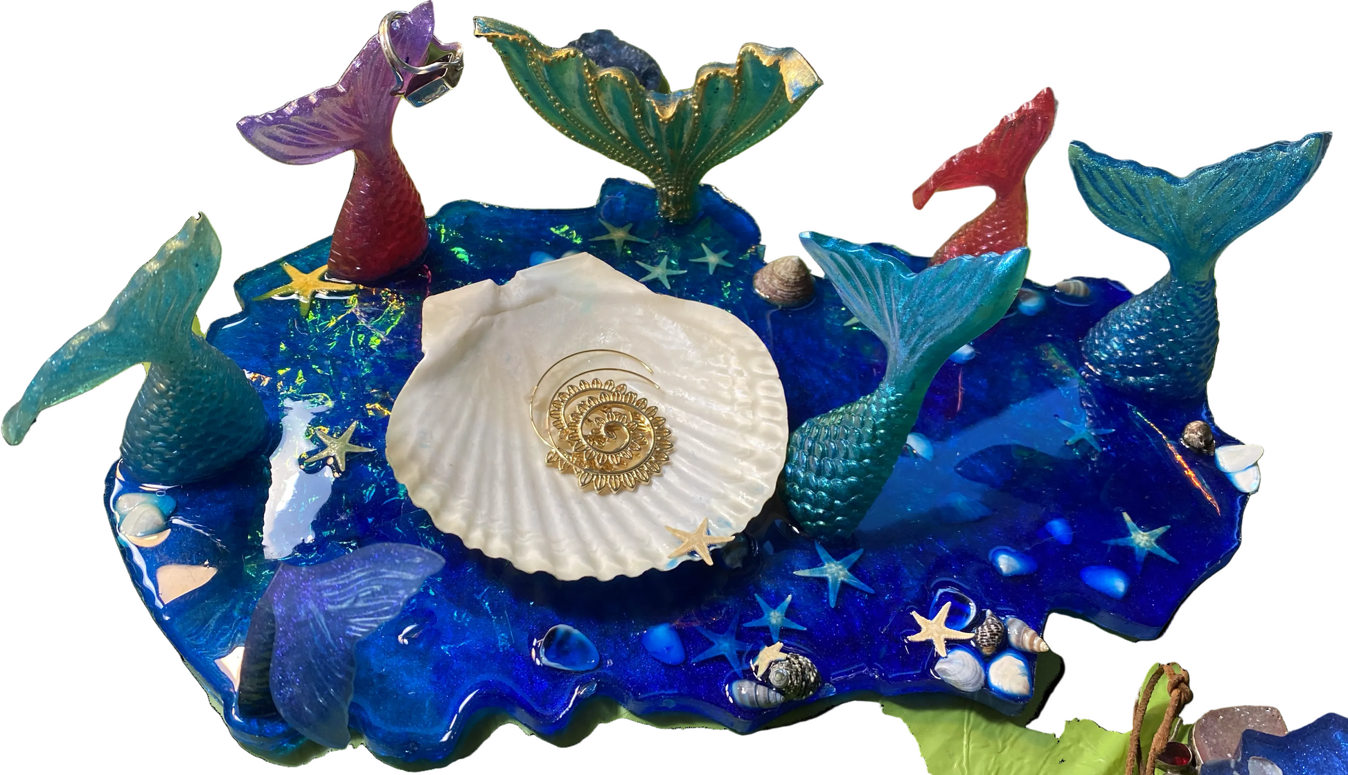 A decorative mermaid-themed resin tray featuring a blue ocean base with multiple colorful mermaid tails, starfish, shells, and a large white seashell in the center, Handmade with love by The Artzy Bubbe